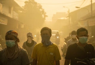 Pontianak residents wearing masks against thick yellow smoke haze on street, midday