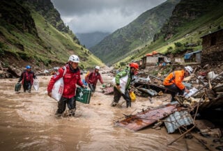 Rescue workers wading through floodwaters in Nepal mountain valley carrying supplies, searching debris