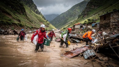 Rescue workers wading through floodwaters in Nepal mountain valley carrying supplies, searching debris