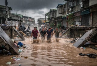 Residents wading through floodwaters on Kaohsiung street during heavy monsoon rain, collapsed walls visible