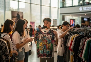 Shoppers browsing clothing in a Shanghai mall, examining graphic apparel under natural light