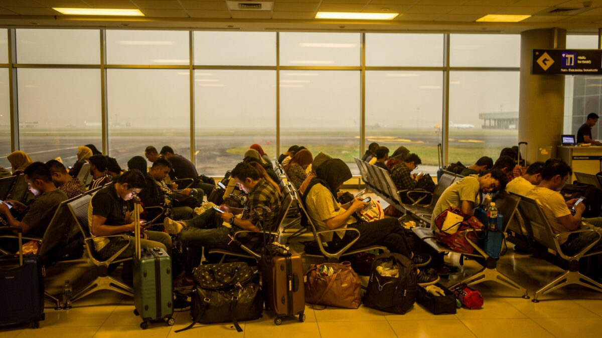 Stranded passengers with luggage in crowded Jakarta airport terminal, volcanic ash haze visible through windows