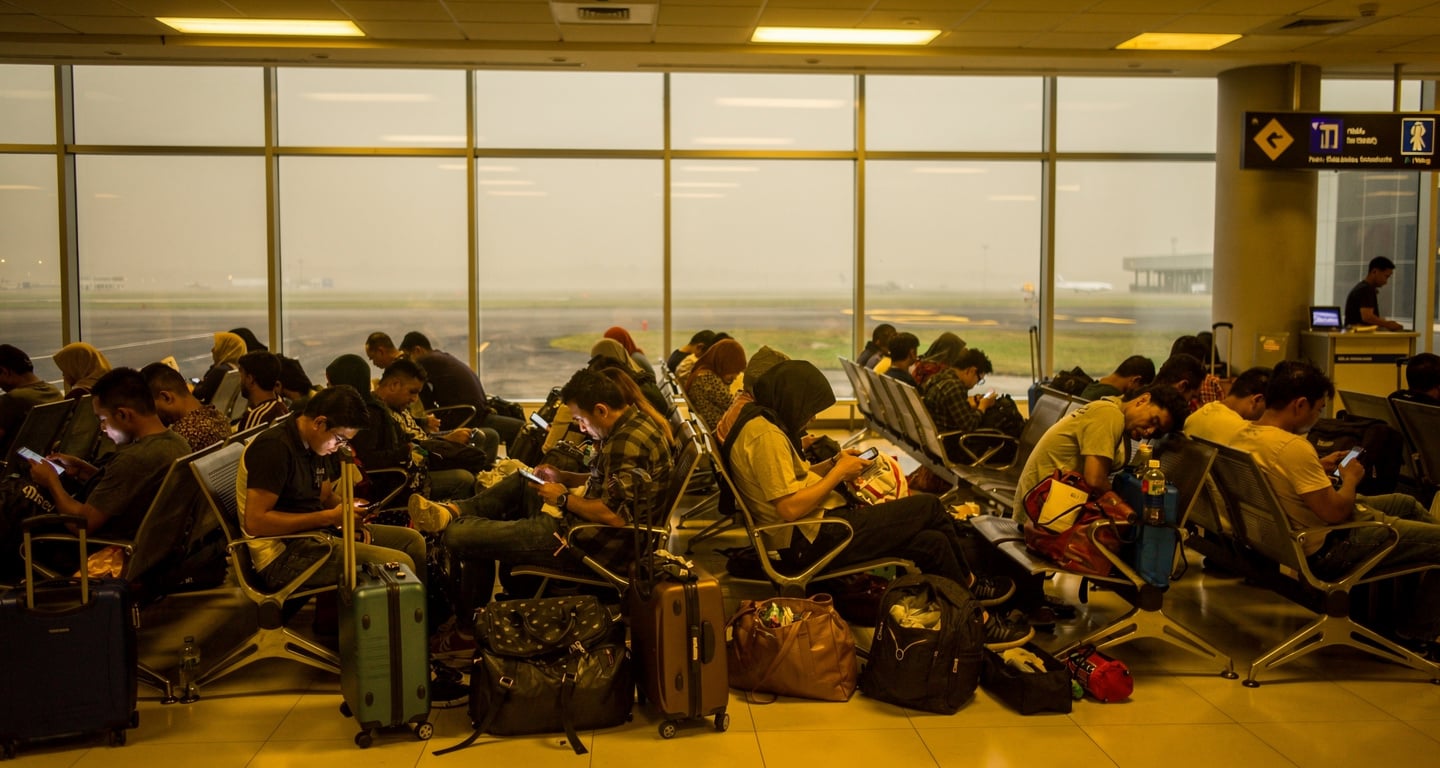 Stranded passengers with luggage in crowded Jakarta airport terminal, volcanic ash haze visible through windows