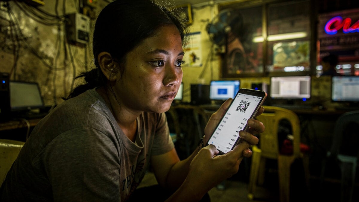 Woman at Manila internet cafe reviewing QR code payment on phone screen at night