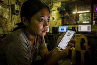 Woman at Manila internet cafe reviewing QR code payment on phone screen at night