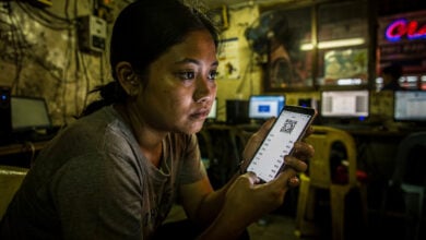Woman at Manila internet cafe reviewing QR code payment on phone screen at night
