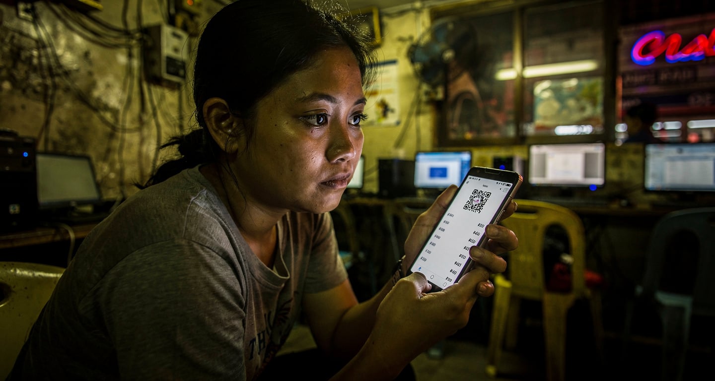 Woman at Manila internet cafe reviewing QR code payment on phone screen at night