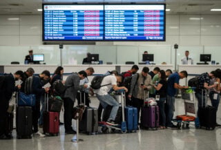 Passengers queueing at a Jeddah airport counter under a cancelled-flights board